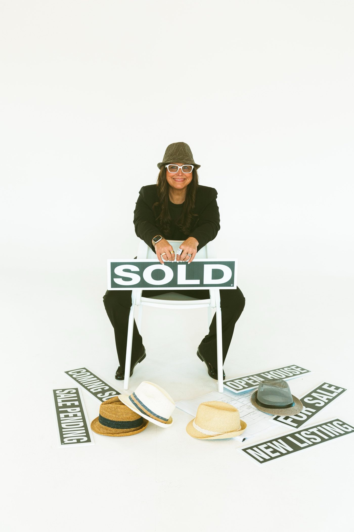 Tara Hayes, Knoxville Realtor and licensed building contractor, seated with a Sold sign and her collection of hats